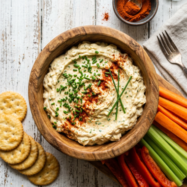 Creamy deviled egg dip in wooden bowl garnished with chives and paprika, surrounded by crackers