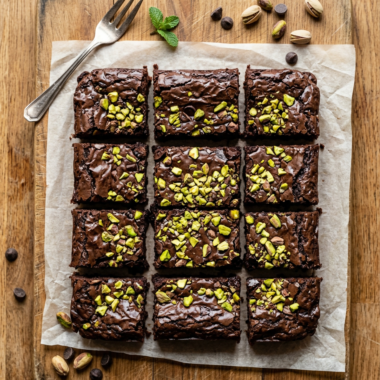 Fudgy pistachio brownies with chopped pistachios on wooden cutting board