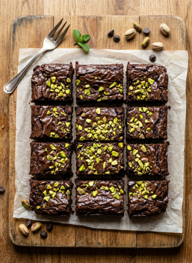 Fudgy pistachio brownies with chopped pistachios on wooden cutting board