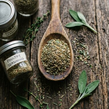 Homemade poultry seasoning recipe blend of herbs in wooden spoon with mason jars