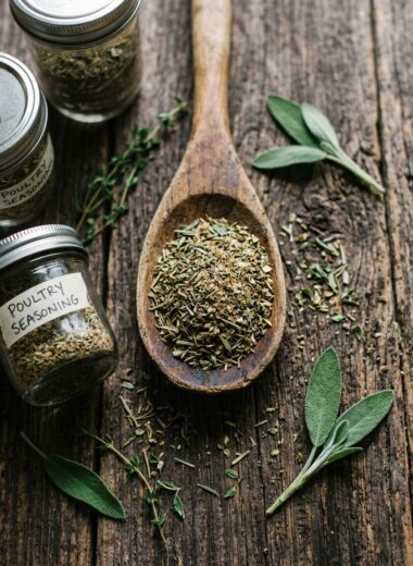 Homemade poultry seasoning recipe blend of herbs in wooden spoon with mason jars