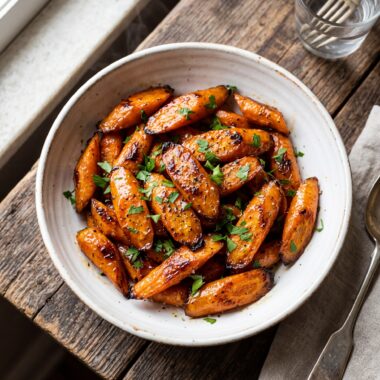 Honey glazed carrots in white bowl with golden glaze and fresh parsley garnish