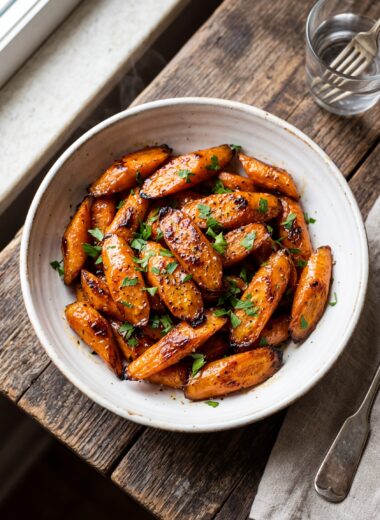 Honey glazed carrots in white bowl with golden glaze and fresh parsley garnish