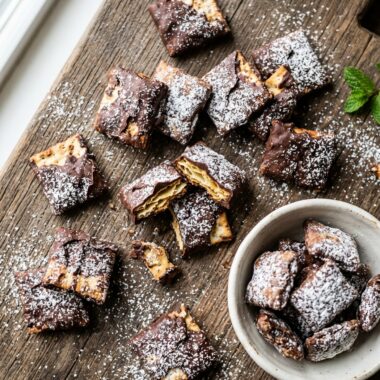 Overhead view of chocolate-coated Matzo Muddy Buddies dusted with powdered sugar on wooden surface