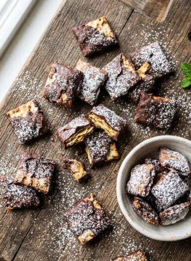 Overhead view of chocolate-coated Matzo Muddy Buddies dusted with powdered sugar on wooden surface